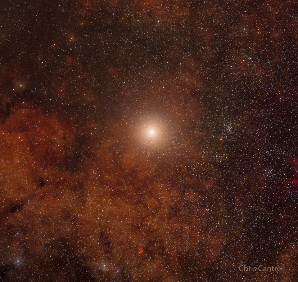 A star field is filled with red-glowing gas. Near the centre
is a bright star system Alpha Centauri, the closest star system to
our Sun.
Please see the explanation for more detailed information.