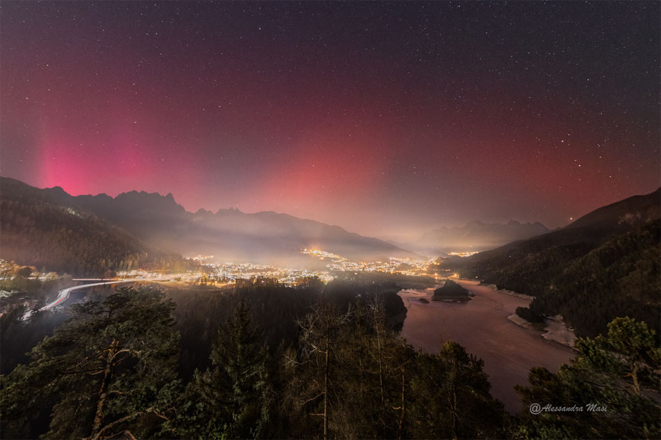 A star field appears above a town at night. The left part
of the sky shows a pinkish-red glow that is an aurora, while the
right part of the sky shows a smoother and darker glow that is
a SAR arc. 
Please see the explanation for more detailed information.