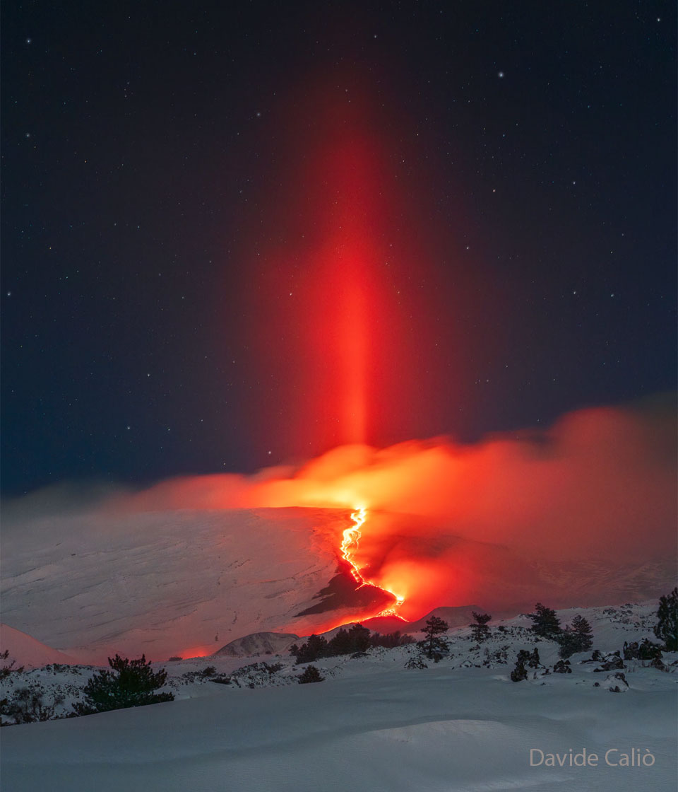 A slope of volcano is pictured with red glowing
lava running down its side. A dark starry sky is in
the background. Up into the sky a red column is visible.
Please see the explanation for more detailed information.