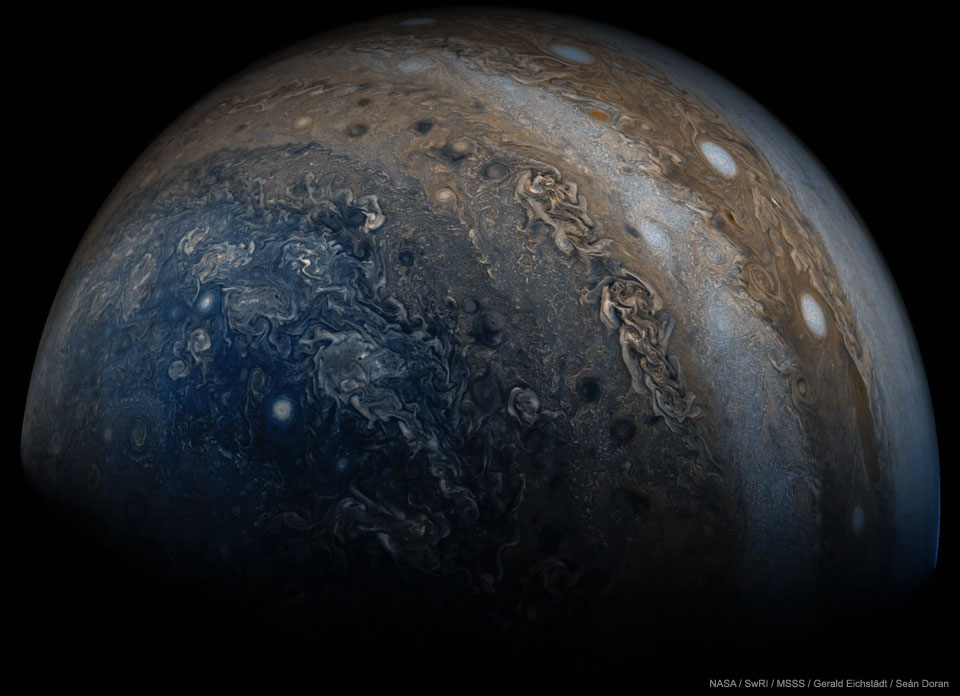 A close-up image is shown of the planet Jupiter.
Many clouds are visible including clouds coloured blue
near the bottom, on the left, and white oval clouds
on the upper right. 
Please see the explanation for more detailed information.