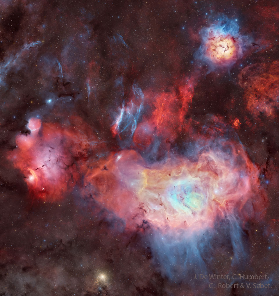 A starfield surrounds a several large nebulae
that appear mostly red but also white and blue.
Dark dust and blue filaments also populate the frame. 
Please see the explanation for more detailed information.