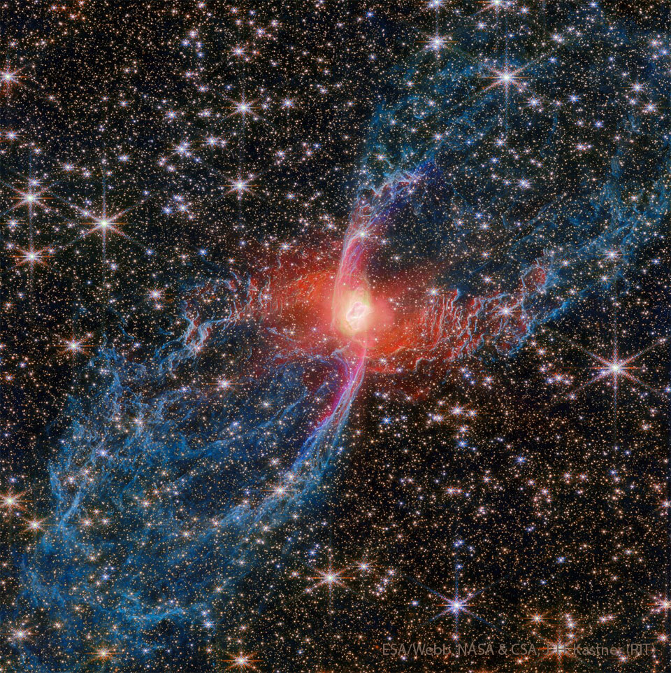 A dense starfield surrounds a blue and red nebula
that stretches from the lower left to the upper right.
The outer parts of the nebula are blue and filamentary,
while the innermost part is red and bright. 
Please see the explanation for more detailed information.