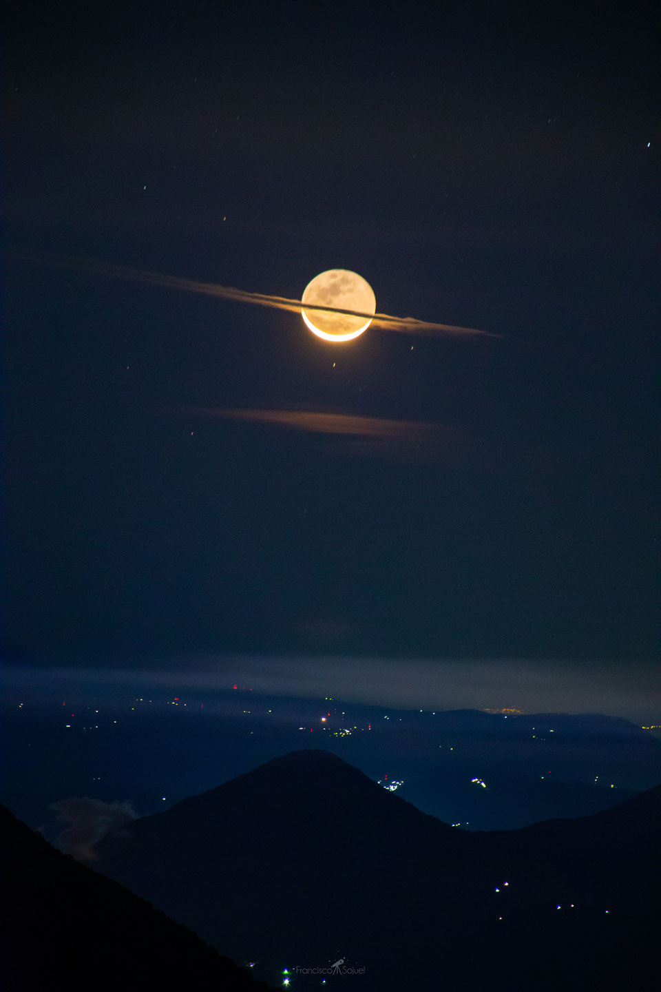 The featured image shows a crescent Moon over a city
and volcano with a flat cloud running through the centre that
makes the Moon like a bit like the planet Saturn.
Please see the explanation for more detailed information.