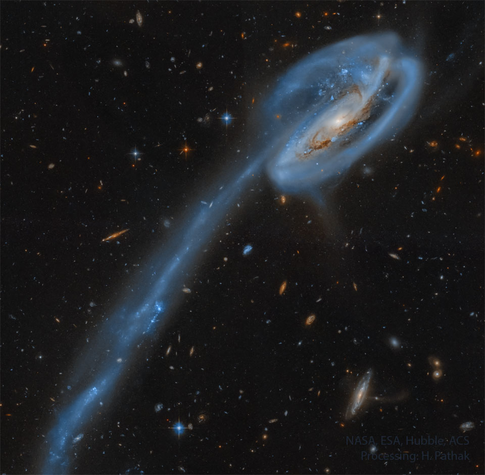 A spiral galaxy is shown on the upper left with a really
long tail of stars and blue-glowing gas trailing to the 
lower left. 
Please see the explanation for more detailed information.