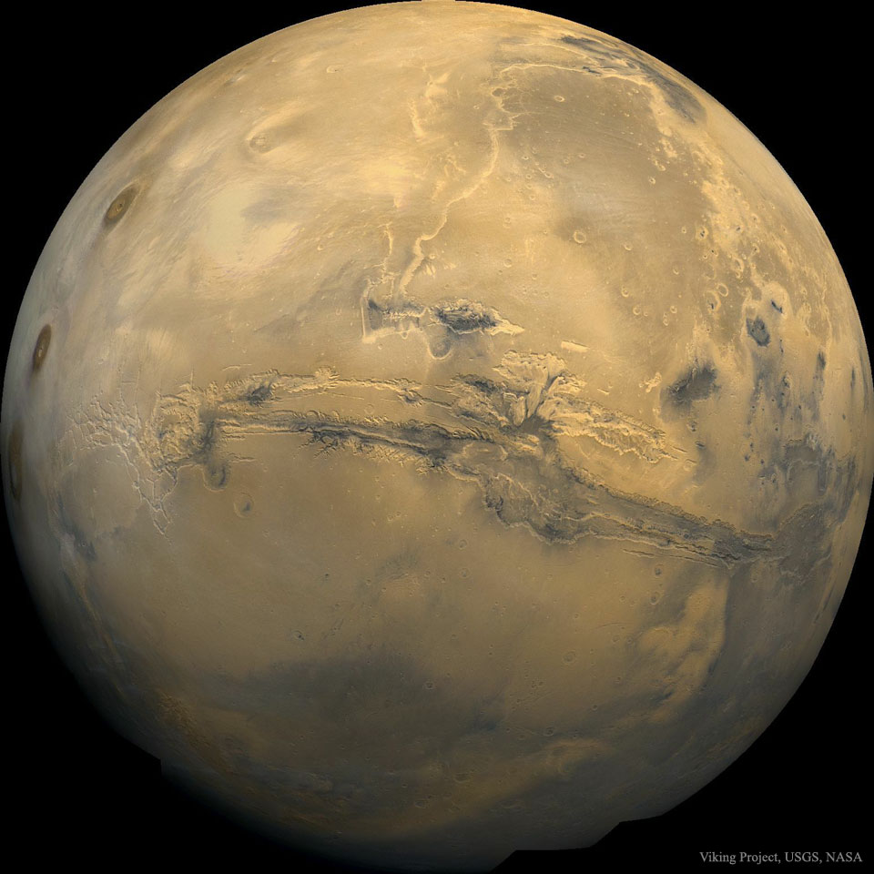 A picture of Mars is shown as a large orange globe.
Across the centre of the planet a long canyon is visible. 
Please see the explanation for more detailed information.