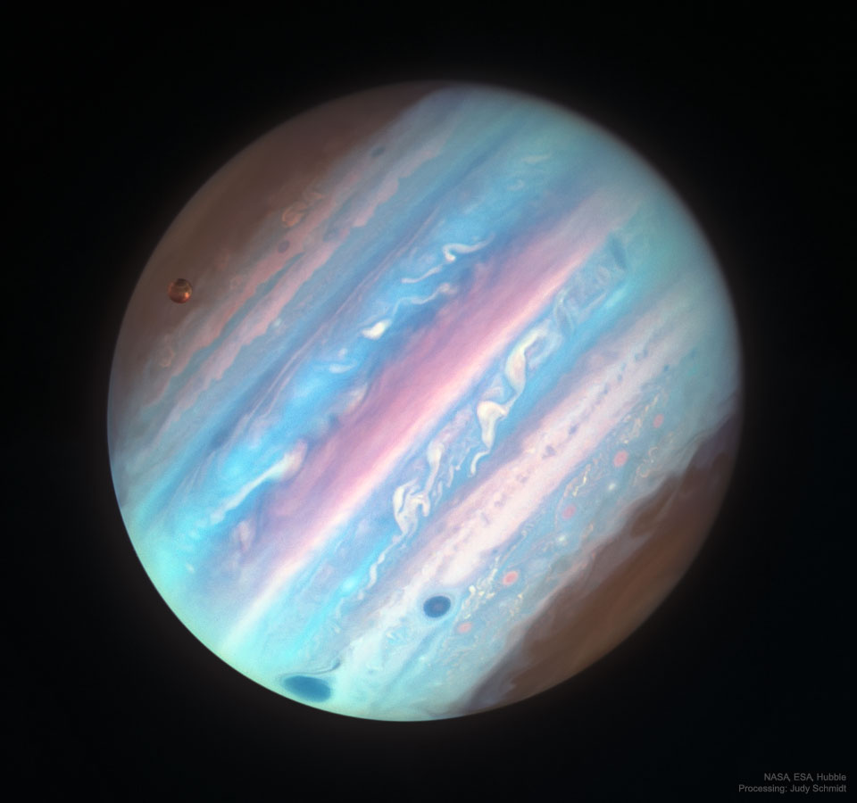 The planet Jupiter appears full frame in apparent colours 
of a variety of blues and some pink bands. The Great Red Spot
is visible on the lower left as a dark spot. Jupiter's Moon
Ganymede is visible on the upper left. 
Please see the explanation for more detailed information.