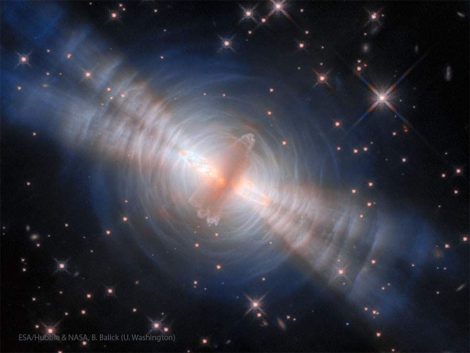 A starfield is shown with an unusual orange object in the centre.
Surrounding this object are blue rings and four thick jets. 
Please see the explanation for more detailed information.