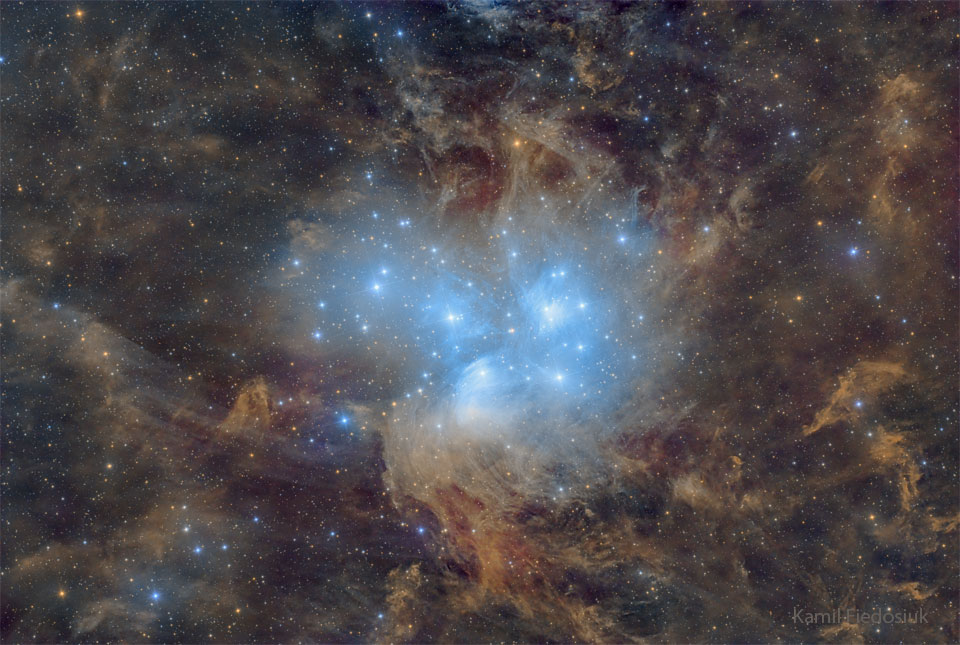 A cluster of blue stars is seen against a starfield
of brown and clumpy dust. The stars illuminate some of 
the nearby dust which causes the dust to glow blue.
Please see the explanation for more detailed information.