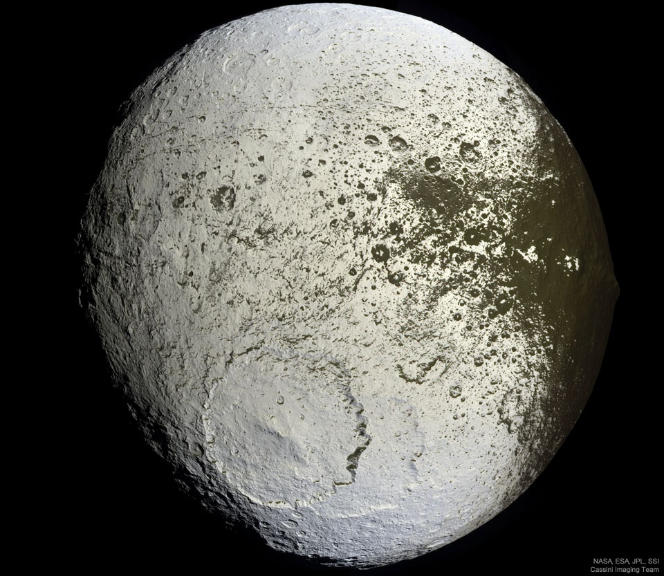 An unusually coloured ball is shown against a 
dark background. The ball has numerous craters but
a very large cratered near the lower centre. Much of
the ball is light coloured, but around the right and
top it is green-brown, with a border area that seems
splattered. 
Please see the explanation for more detailed information.