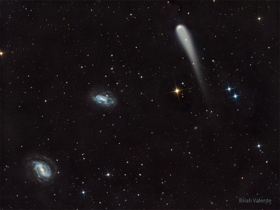 A picture shows a starfield with three prominent objects.
A blue spiral galaxy is on the lower left and another blue spiral
is just left of centre. Toward the upper right is a light-coloured
comet with a tail fading toward in the image bottom.
Please see the explanation for more detailed information.