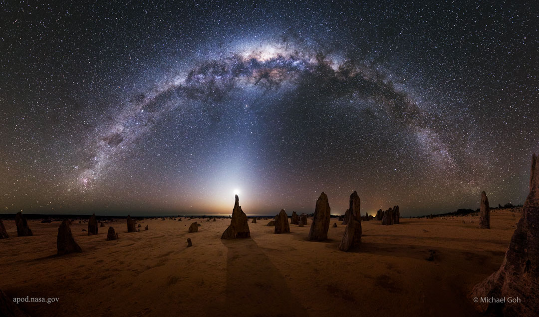 A flat landscape is shown at night that appears mostly
brown. Numerous unusual rock spires are seen rising from the 
group. Above, a full star field is seen with the arch of our 
Milky Way Galaxy curving from left to right. 
Please see the explanation for more detailed information.