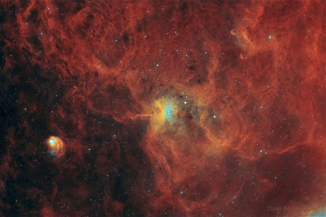 A star field has a red diffuse glow on the right-hand side.
Distinct nebulae appear in the centre and on the lower left. 
Please see the explanation for more detailed information.