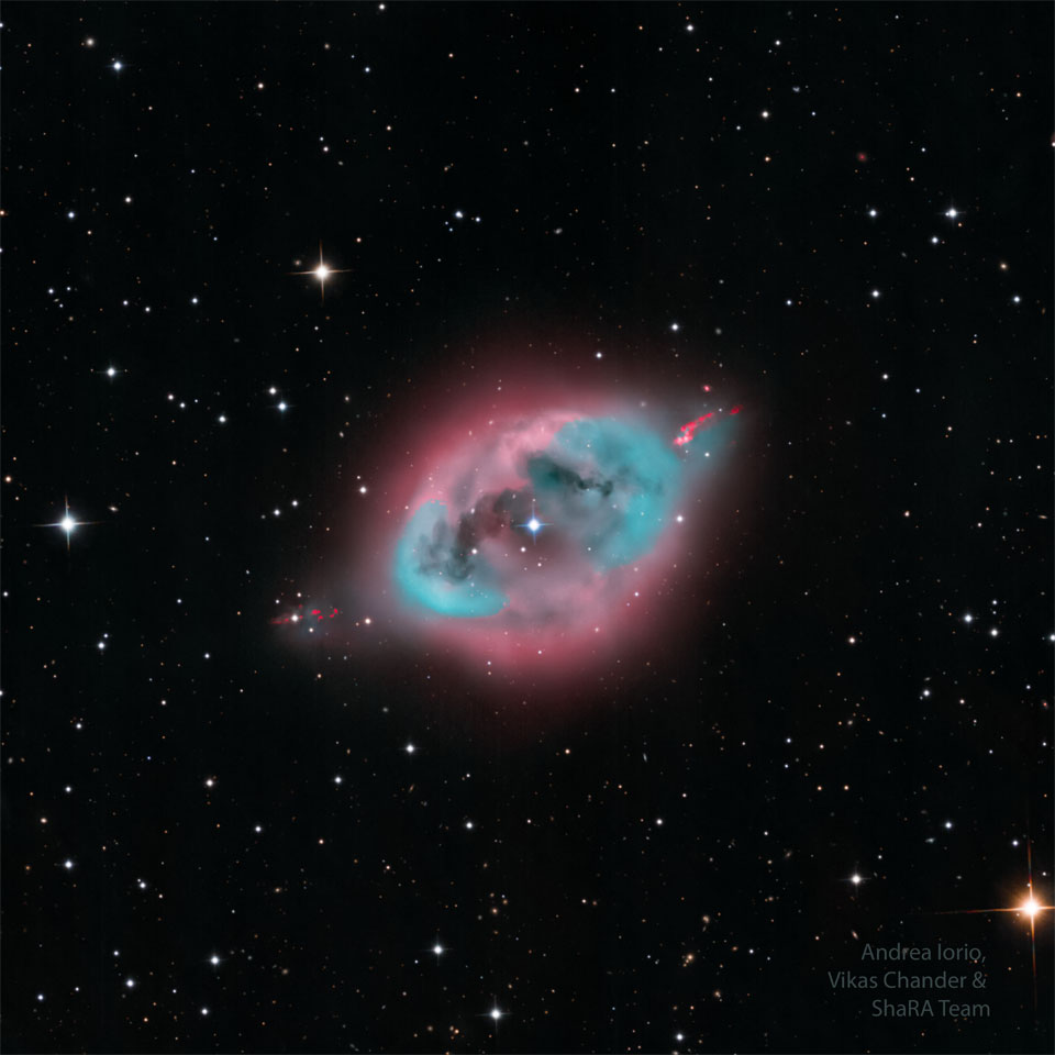 A dark starfield highlights a blue and pink nebula
in its centre. Some dark lanes of dust are seen inside
nebula's centre. 
Please see the explanation for more detailed information.