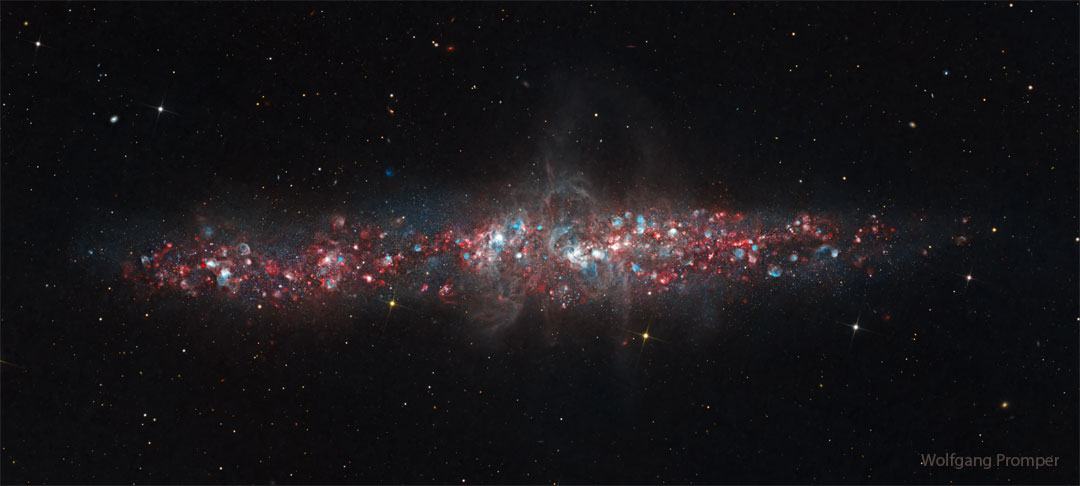 A galaxy is shown that has a lot of blue and red dots in it. The 
galaxy is an long elliptical blob across the middle and not a classic spiral. 
Please see the explanation for more detailed information.