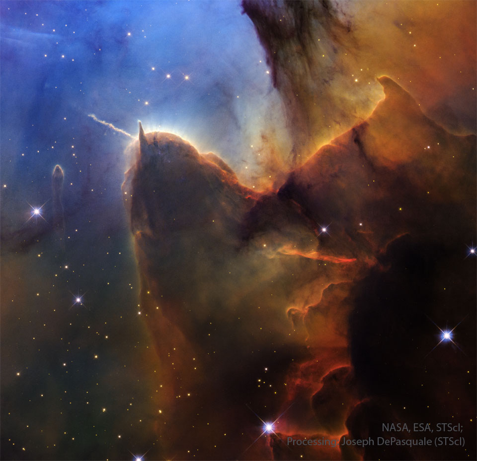 A field of stars on the left is mirred by a wall of
opaque brown dust on the right. Jutting out from the wall is
a long pillar with a rounded end that has a prominent light-
coloured jet emanating toward the upper left. The stellar 
background toward the upper left is dark blue.
Please see the explanation for more detailed information.