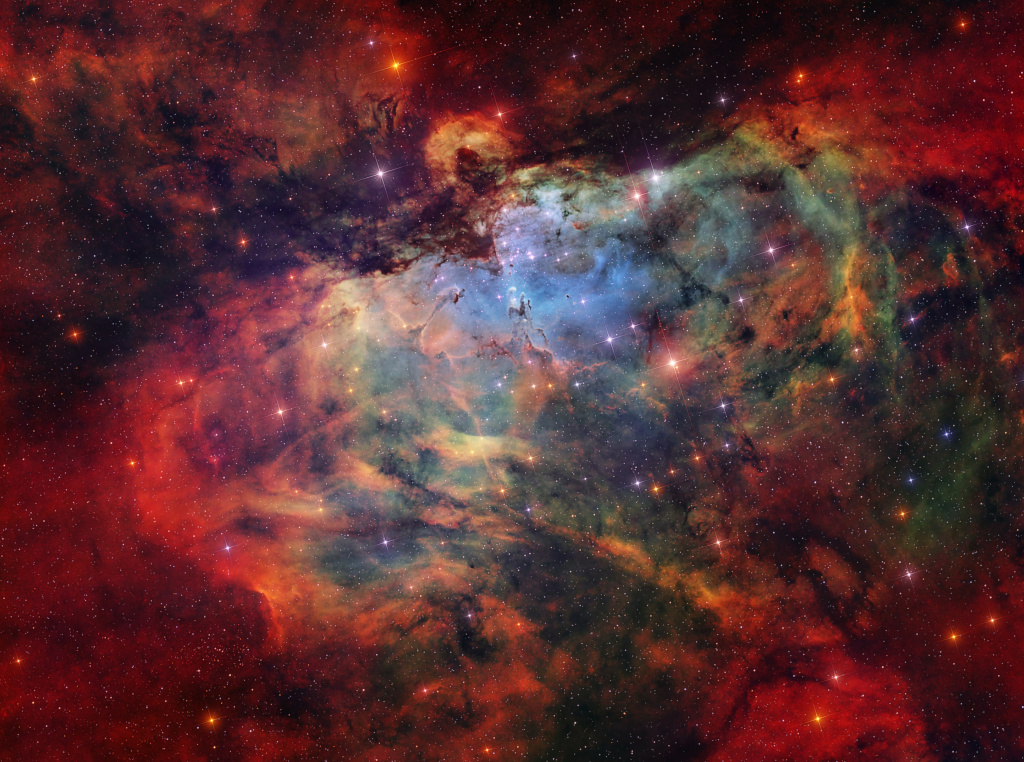 Gas, dust, and stars are scattered across the image. A dark silhouette that looks like an eagle swoops downward towards three small pillars 
of gas. Other gas and dust pillar-like features reach out of the surrounding nebula. A central cluster of stars sits beneath the eagle silhouette.