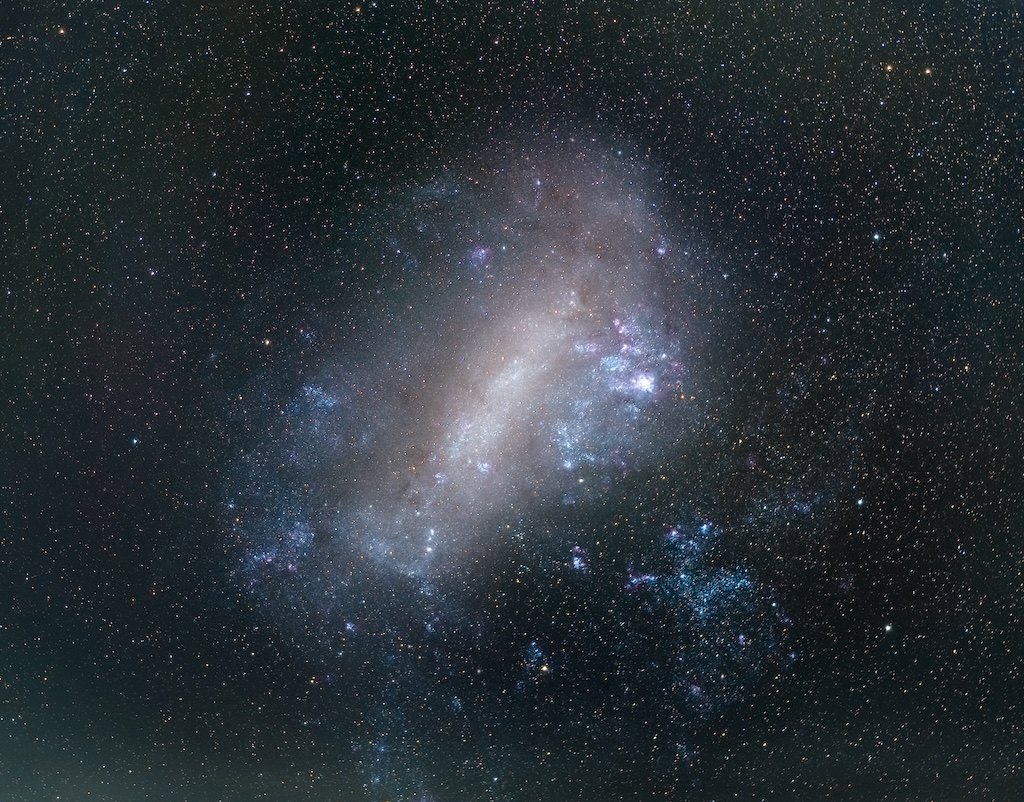 A galaxy with stars and colourful clous of gas.
	  The background is a dark field of stars. 