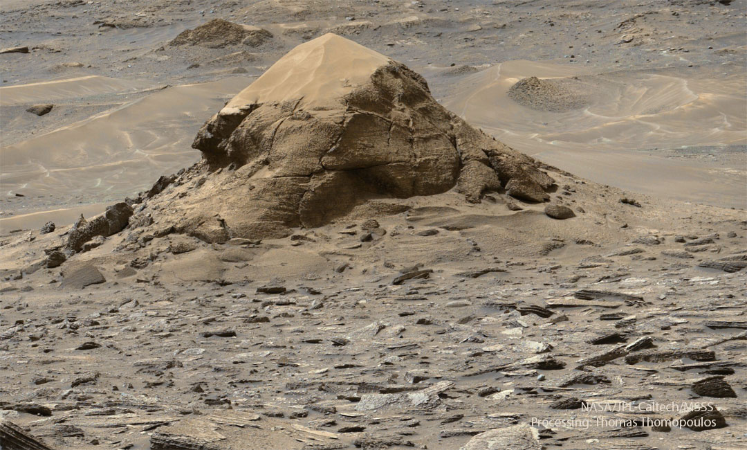 An orange landscape is seen with many darker rocks
visible in the foreground. Toward the image top is a large
rock outcrop with orange sand on top. The outcrop may appear
to resemble a large turtle.
Please see the explanation for more detailed information.